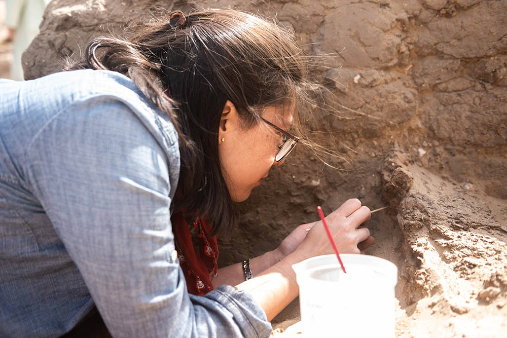Close up photograph of conservator excavating coffin with small tools.