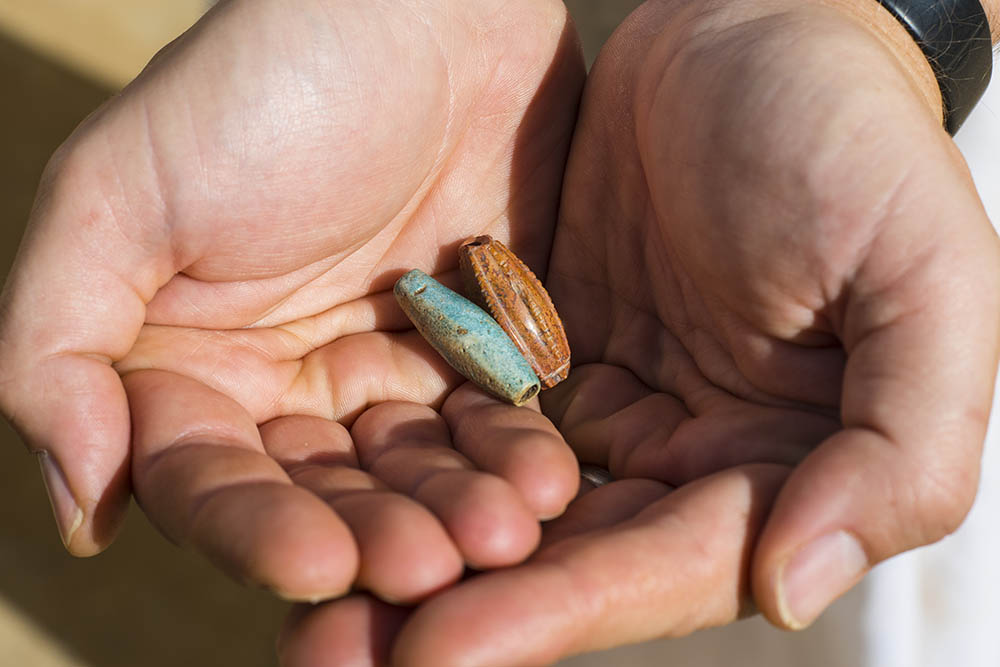 close up of hands holding two beads recovered from the temple.