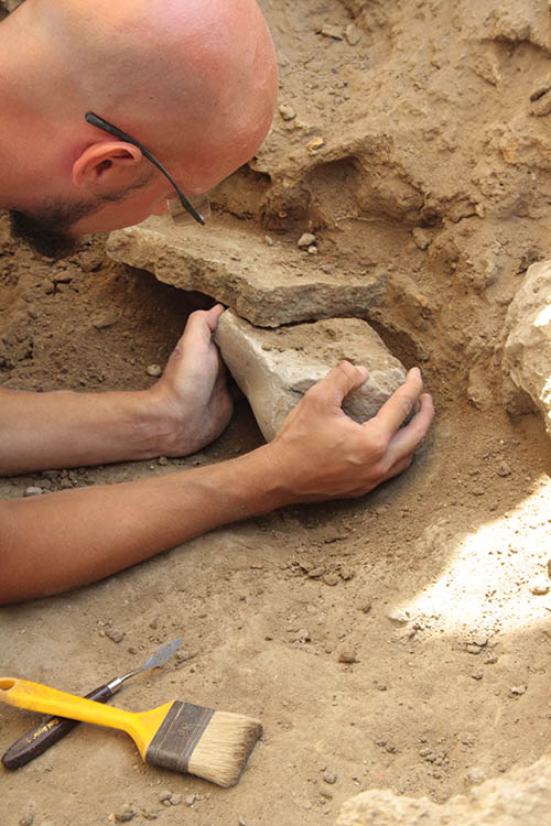 Close up view of two hands removing a large fragment from the dirt.