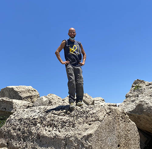 Luca Restelli standing on a large rock with a blue sky in the background.