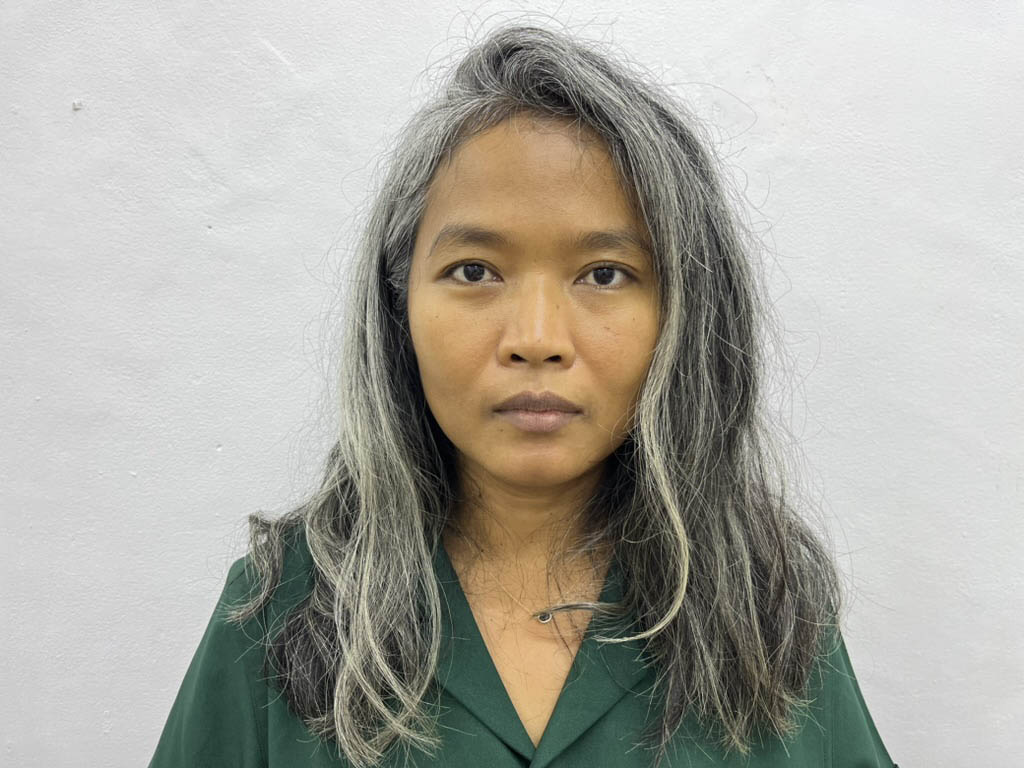 Portrait of the artist in front of a white wall.