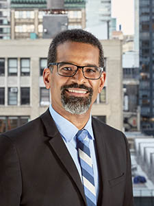 portrait of Angel Ayón with tall building in the background.