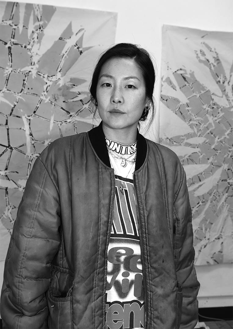 Black and white portait of the artist in front of her work.